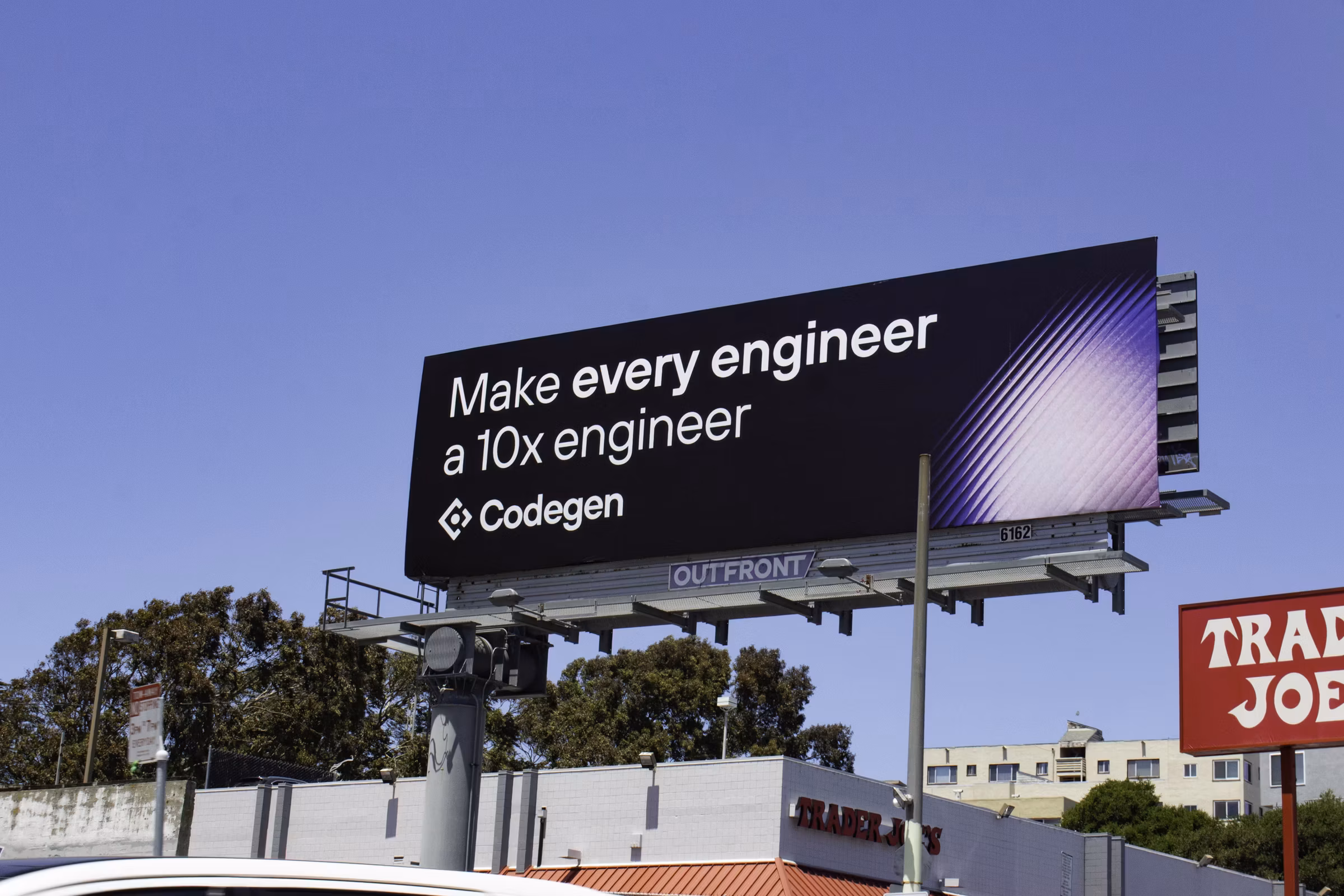 A roadside bulletin against a blue sky - 'Make every engineer a 10x engineer' with the Codegen logo and a purple gradient - rising above a Trader Joe's.