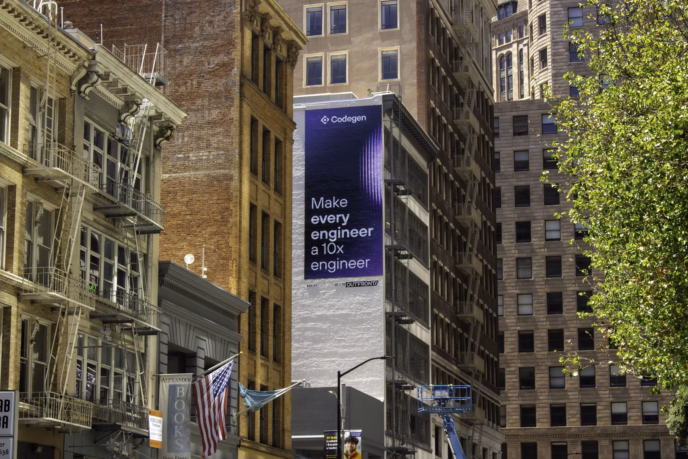 A tall vertical wallscape on the side of a downtown San Francisco building - 'Make every engineer a 10x engineer' over a purple gradient - among brick facades and fire escapes.